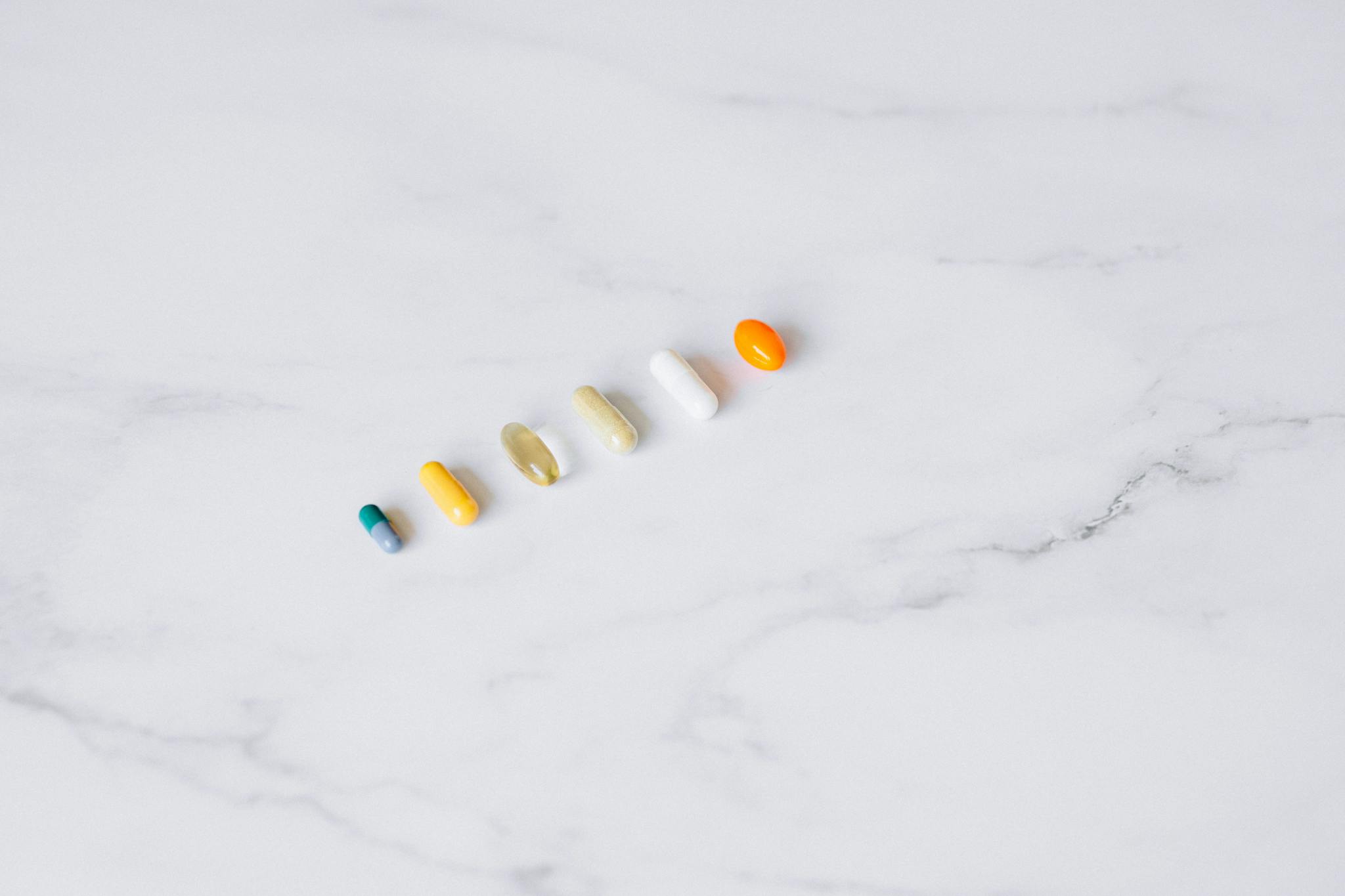 Aerial view of assorted capsules arranged on a white marble surface.