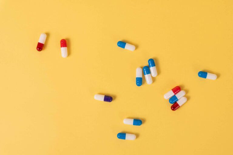 Colorful medication capsules scattered on a vivid yellow background, ideal for health-related themes.
