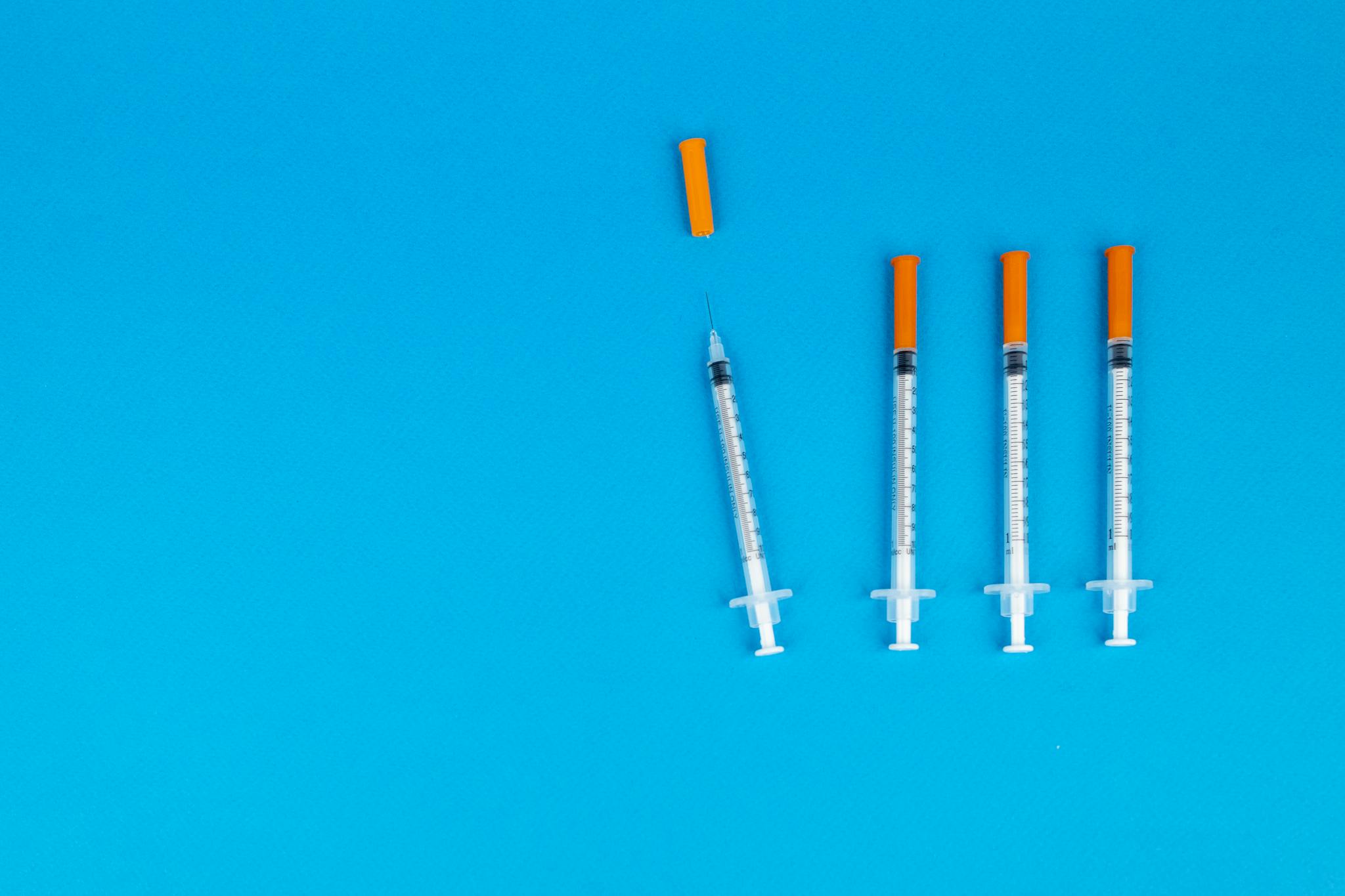 Four medical syringes with orange caps on a vivid blue background, ideal for healthcare or vaccination themes.